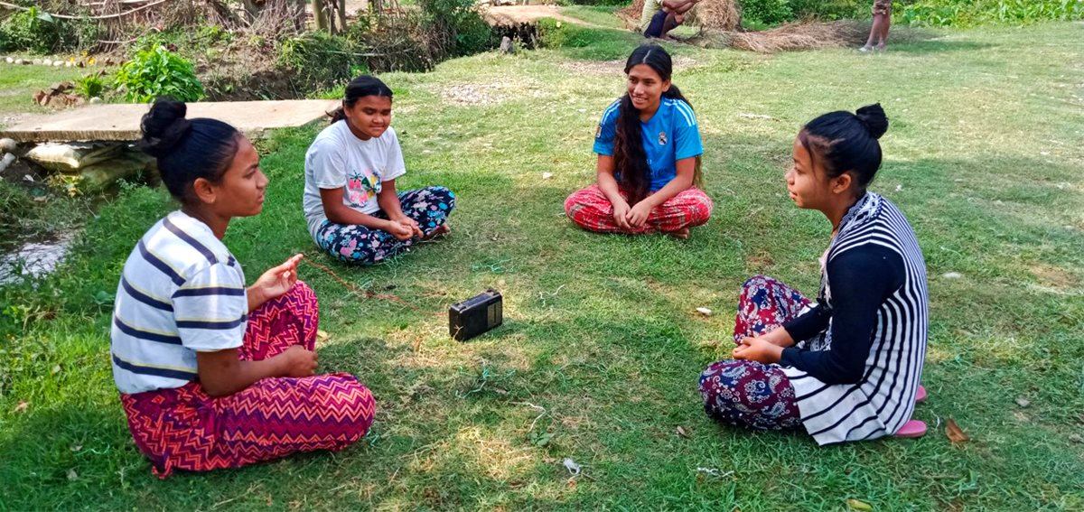 Jenter fra Nepal sitter i ring rundt en radio og hører på Radio Damvad.